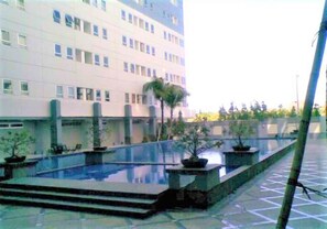 A building with a pool area, including steps leading to the pool and potted plants. - Apartement Puncak Permai Tower A by Nur Faizah (Surabaya)