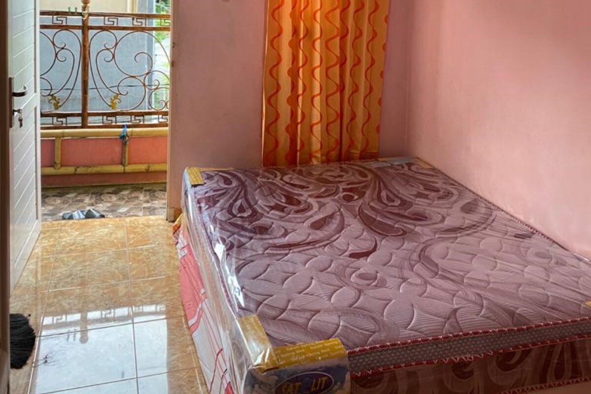 A small room with a bed, an air conditioner, a window with a curtain, and a view of a balcony.