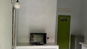 A room with a white bench, a microwave on the bench, a green door, and a small refrigerator. - Wisma Adhyaksa 2 (Makassar)