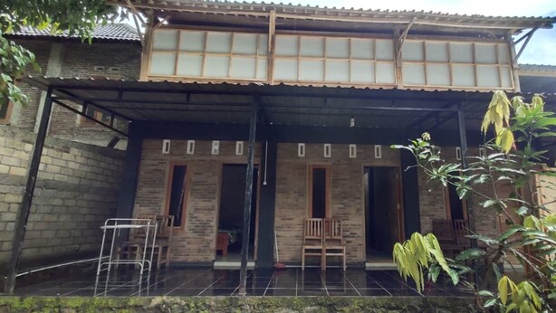 A traditional two-story building with a tiled porch, wooden benches, and a metal chair. - Homestay Kurnia - Hostel (Muntuk)