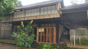 A traditional wooden house with a tiled roof, a wooden porch, and a small garden area with plants. - Homestay Kurnia - Hostel (Muntuk)