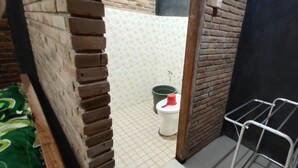 A small bathroom with a toilet, a green bucket, and a metal drying rack. - Homestay Kurnia - Hostel (Muntuk)