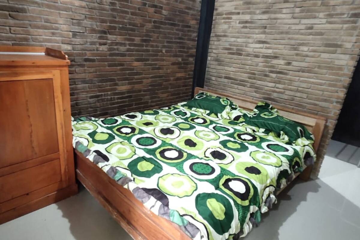Un dormitorio con pared de ladrillo, un armario de madera y una cama con colcha verde y blanca.