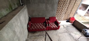A room with a red sofa, a patterned curtain, and a concrete floor. - Homestay Kurnia - Hostel (Muntuk)