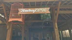 A wooden structure with a sign reading "Homesraykurnia" and two birdcages hanging from the ceiling. - Homestay Kurnia - Hostel (Muntuk)