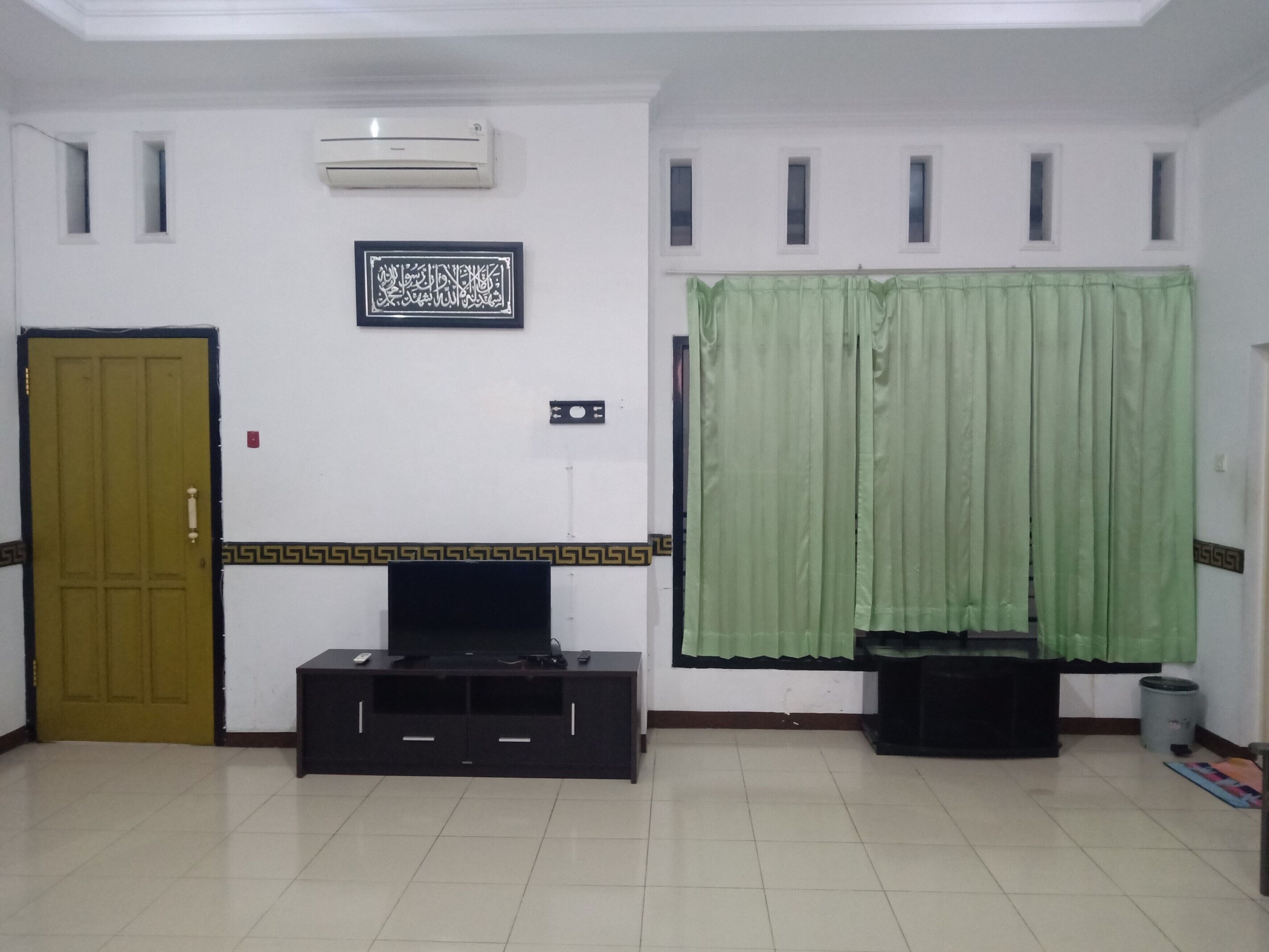 A room with a closed door, a flat-screen TV on a black stand, an air conditioner, and a green curtain.