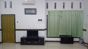 A room with a closed door, a flat-screen TV on a black stand, an air conditioner, and a green curtain.