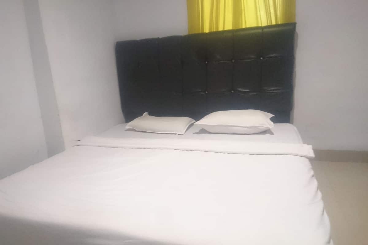 A small, neatly made bed with white linens and two pillows, a dark headboard, and a yellow curtain partially visible.