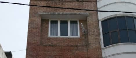 Um edifício de dois andares em tijolo, com telhado plano e uma pequena varanda no segundo andar.