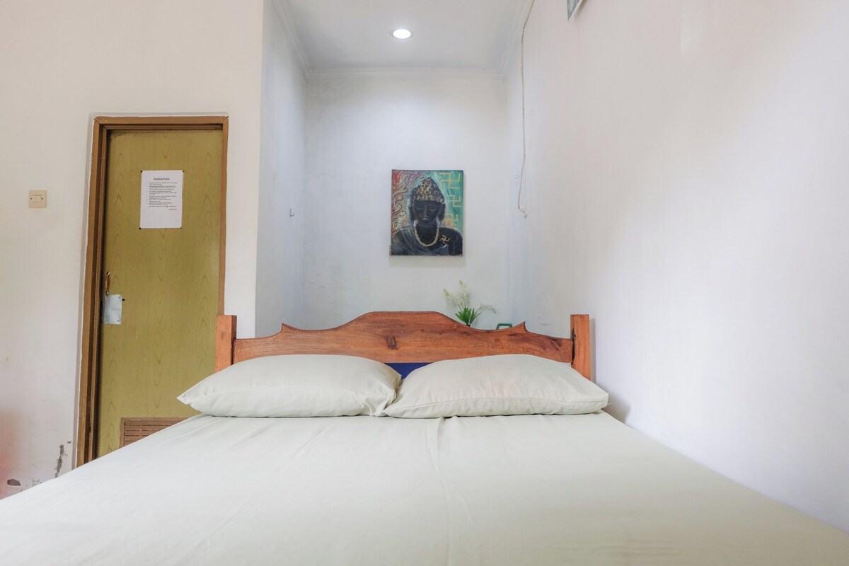 A bedroom with a wooden headboard, two white pillows, and a painting on the wall.