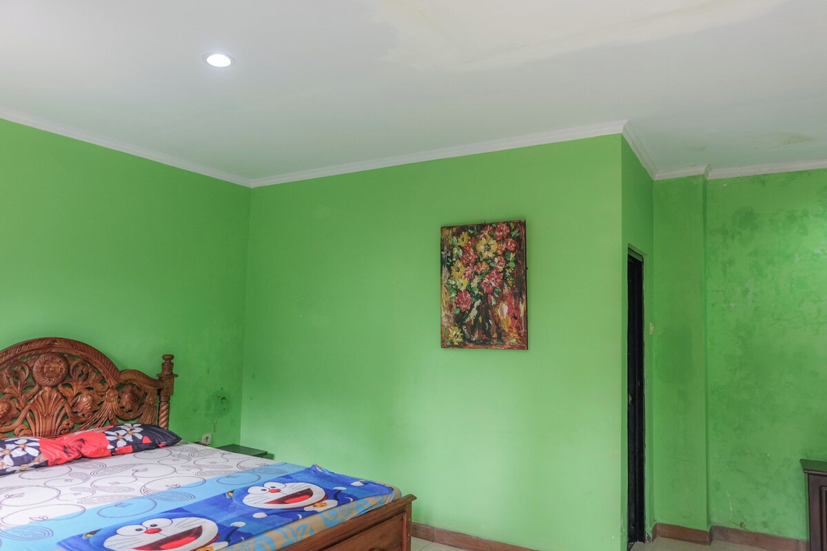 Un dormitorio con pared verde, estructura de cama de madera, una pintura floral y una puerta a otra habitación.
