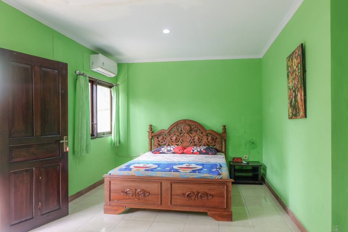 A bedroom with green walls, a wooden bed with a floral headboard, a window with green curtains, and a painting on the wall.