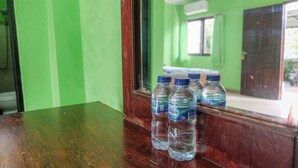 A room with green walls, a wooden table with water bottles, and a window with a view of the outside. - Umah Hijau Tabanan (Tabanan)