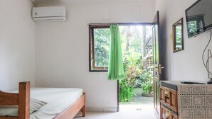 A room with a bed, a small desk with drawers, an air conditioning unit, and a window with a green curtain. - Umah Hijau Tabanan (Tabanan)