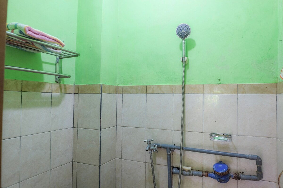 A bathroom with green walls, a tiled floor, a shower with a handheld showerhead, and a towel rack with colorful towels.