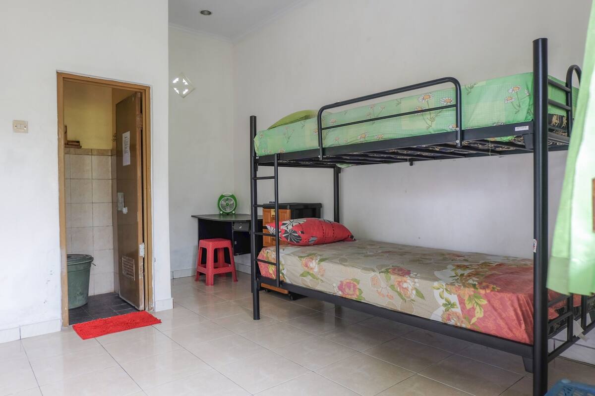 A bunk bed room with a desk and chair, a red mat, and a green trash bin.