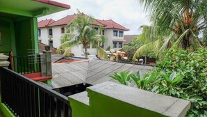 A residential area with a green building, a red-roofed house, and a covered patio area with umbrellas. - Umah Hijau Tabanan (Tabanan)