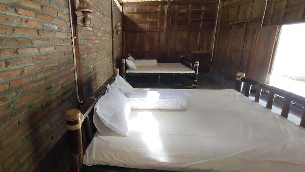 A room with two beds, a brick wall, and wooden paneling. - Omah Regeng (Sumbermulyo)