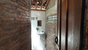 A narrow hallway with exposed brick walls and a tiled floor. A white sink and a mirror are visible in the background. - Omah Regeng (Sumbermulyo)