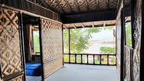 Habitación tradicional con techo de paja, paredes de bambú y vistas al verdor exterior.