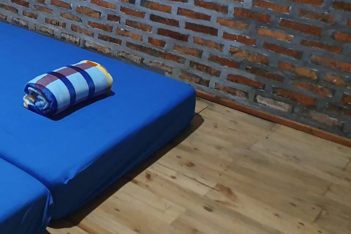 Ett rum med två sängar täckta med blå lakan, en tegelvägg och ett trägolv.