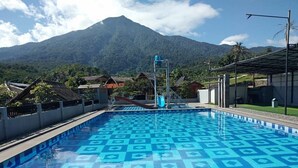Una piscina con un diseño geométrico de azulejos, rodeada por una valla, y una montaña al fondo.