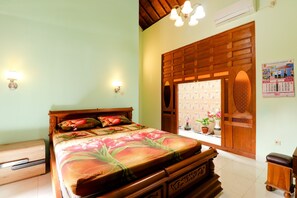 A bedroom with a wooden bed, a nightstand, a dresser, a window with a view, and a wall calendar. - Griya 90TR Syariah (Ngaglik)