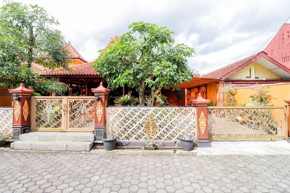 A traditional building with a red roof, a decorative gate, and a tree in front. - Griya 90TR Syariah (Ngaglik)