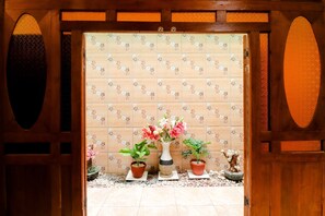 A traditional Japanese interior with a wooden door, a tiled wall with floral patterns, and three potted plants with flowers. - Griya 90TR Syariah (Ngaglik)