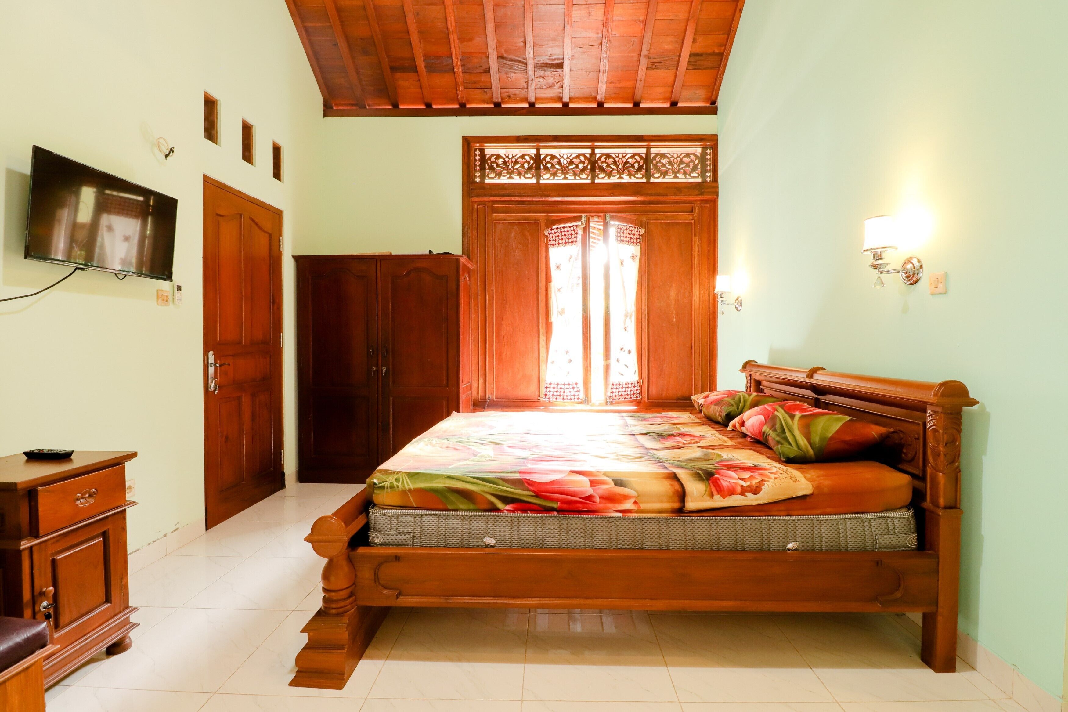 A bedroom with a wooden bed, a television on the wall, and a wardrobe.