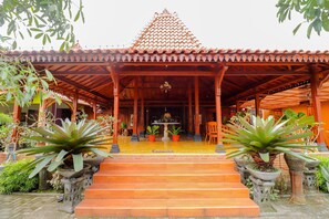 A traditional building with a tiled roof, a covered entrance, and a staircase leading up to a central area with a table and chairs. - Griya 90TR Syariah (Ngaglik)