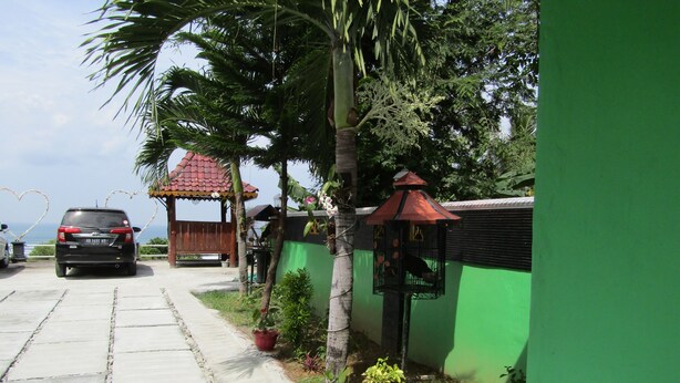 A paved pathway leading to a wooden structure with a red roof, surrounded by greenery and a parked car. - Losmen Kinasih Puncak & Gazebo Pandang by Zuzu (Parangtritis)