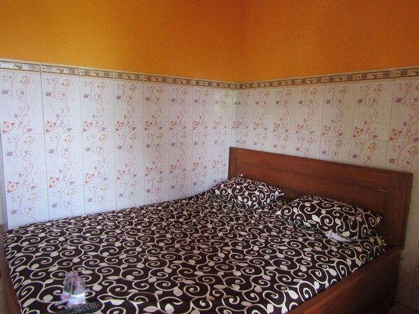Ein Einzelbett mit gemustertem Bettbezug und passenden Kissen in einem Zimmer mit Blumenpapier und einem hölzernen Kopfteil.