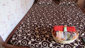 A neatly made bed with a patterned bedspread and pillows, a basket with a towel, and floral wallpaper. - Losmen Kinasih Puncak & Gazebo Pandang by Zuzu (Parangtritis)