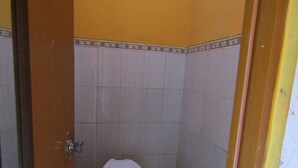A small, narrow bathroom with a toilet and a blue bucket. - Losmen Kinasih Puncak & Gazebo Pandang by Zuzu (Parangtritis)