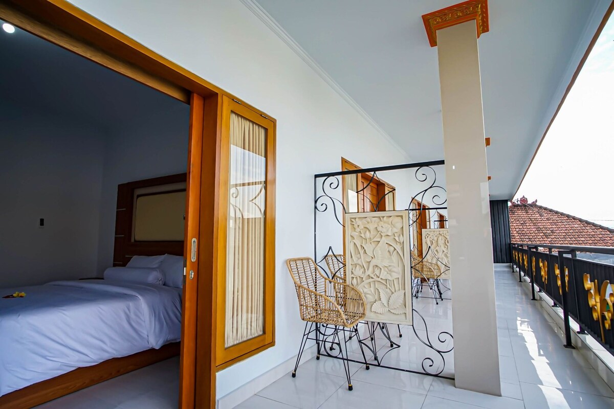 Habitación de hotel con cama, puerta de madera, balcón con barandilla y un separador decorativo.
