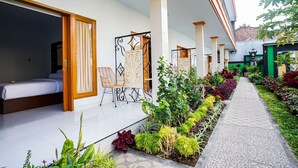 A hotel corridor with a bed, a seating area, and a garden path. - Bagus Kadek Guesthouse (Jimbaran)
