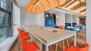 Ein modernes Interieur mit einem langen Gemeinschaftstisch, leuchtend orangefarbenen Stühlen und einem farbenfrohen Deckengestaltung.