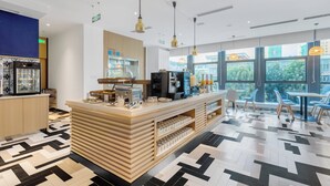 Ein modernes Café mit einer zentralen Theke, Kaffeemaschinen und Blick auf die Stadt durch große Fenster.