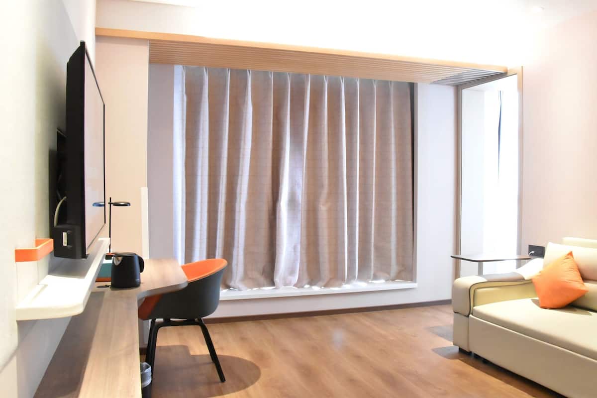 A modern living room with a sofa, a TV, a window with curtains, and a wooden floor.