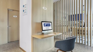 Ein Empfangsschalter mit einem Computermonitor, der den Namen eines Hotels anzeigt, einem Stuhl und einer Holztür mit einem Schild.