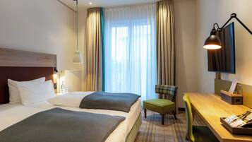 A hotel room with two beds, a desk, a chair, a TV, and a window with curtains.