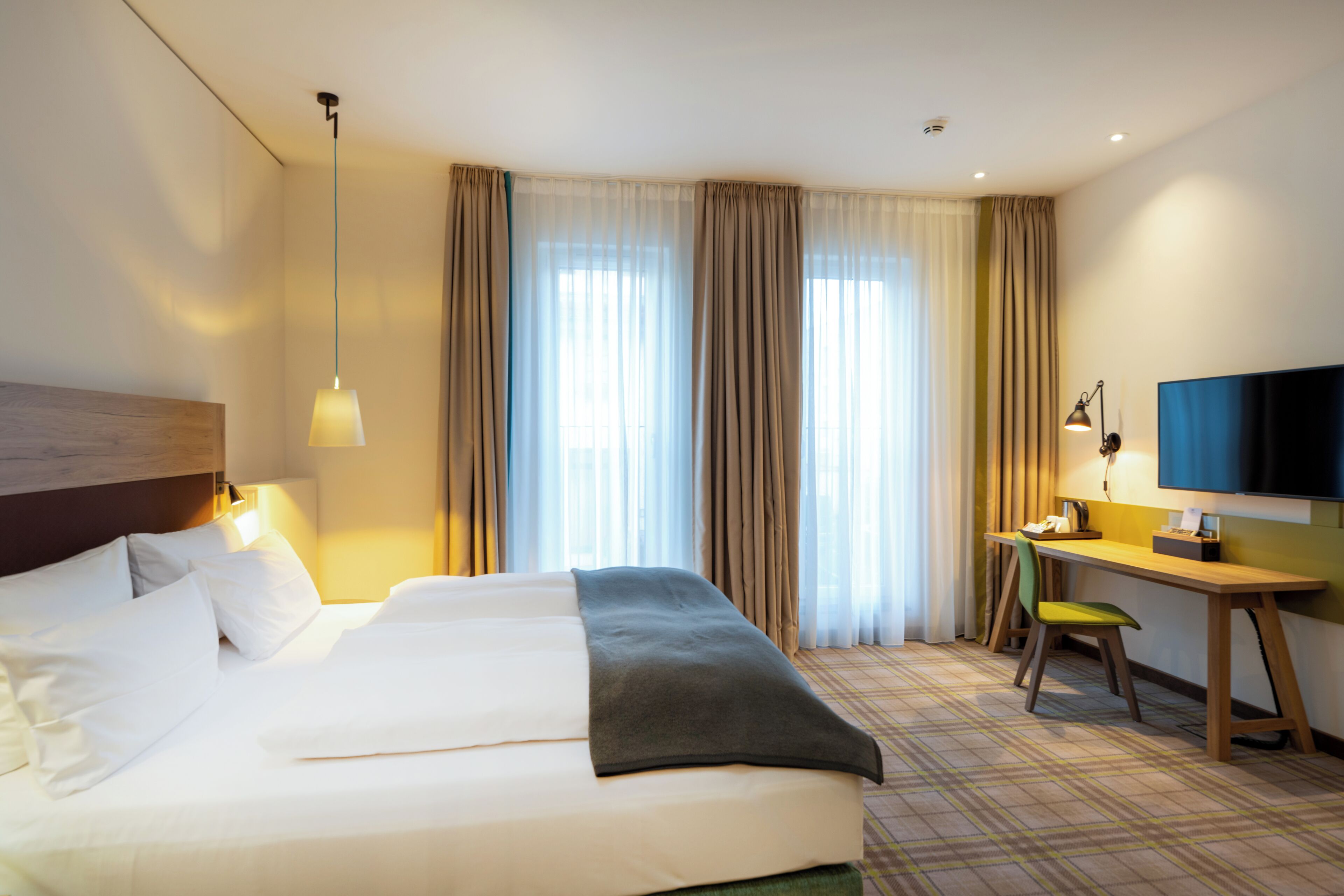 Une chambre d’hôtel avec un grand lit, un bureau avec une chaise, une télévision et des rideaux.