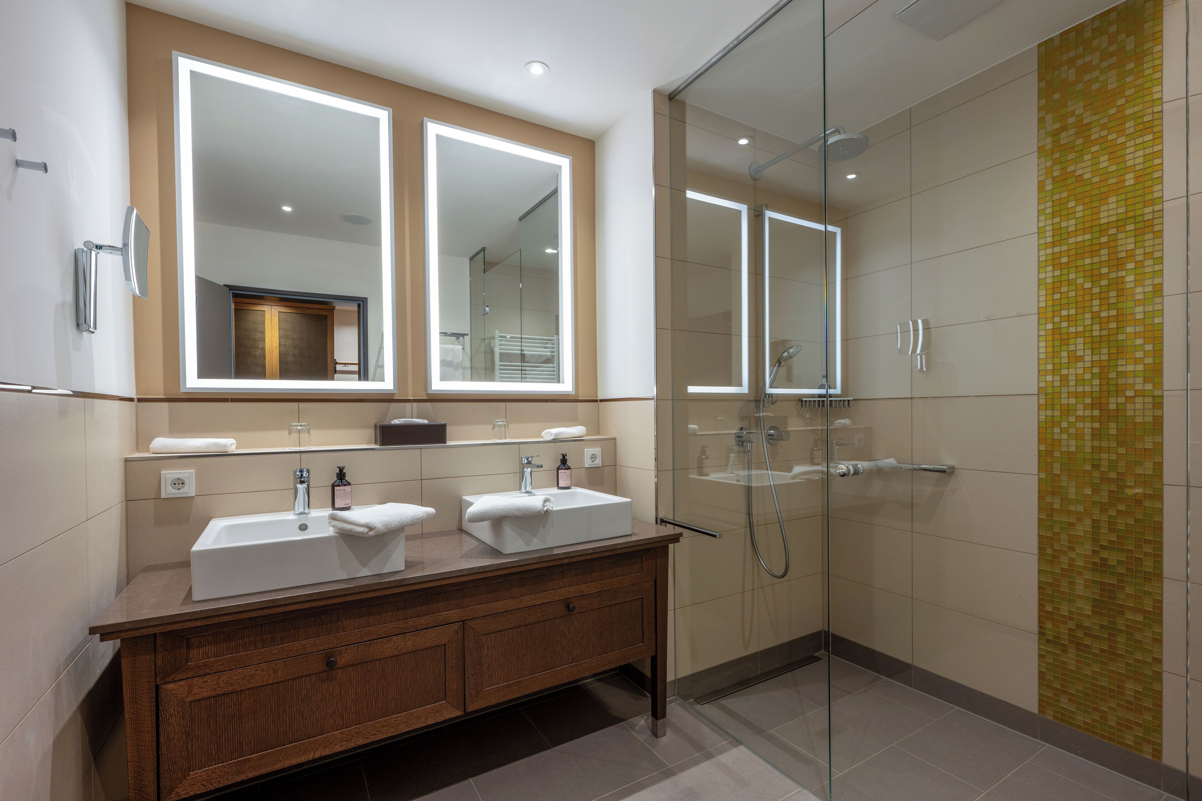 A modern bathroom with two sinks, a large mirror, and a glass-enclosed shower.