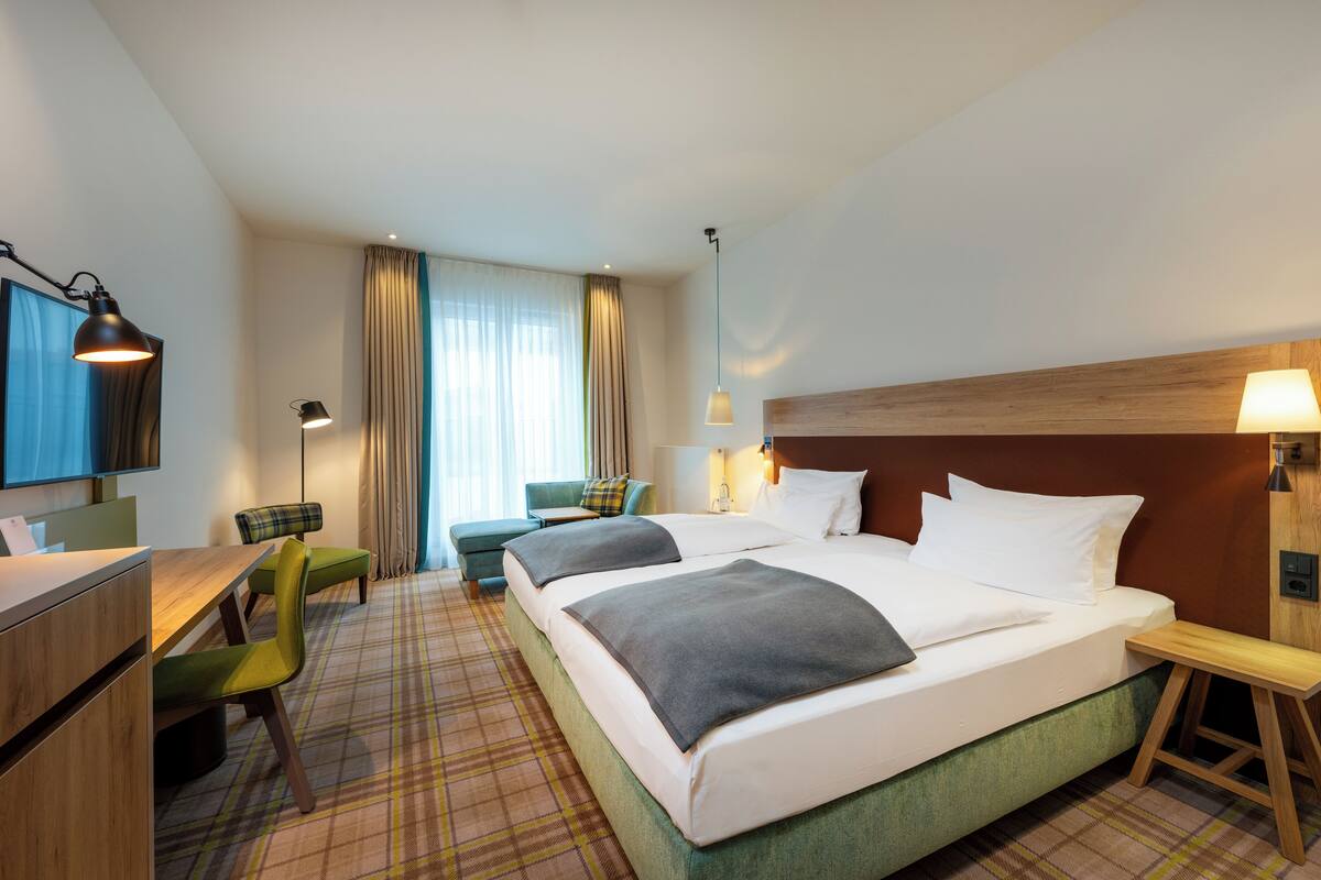 Habitación de hotel con una cama grande, un escritorio, una silla, un televisor y una ventana con cortinas.