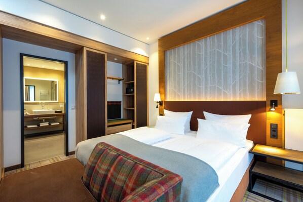 A hotel room with a large bed, a wooden headboard, a nightstand, a lamp, and a wardrobe with a mirror.