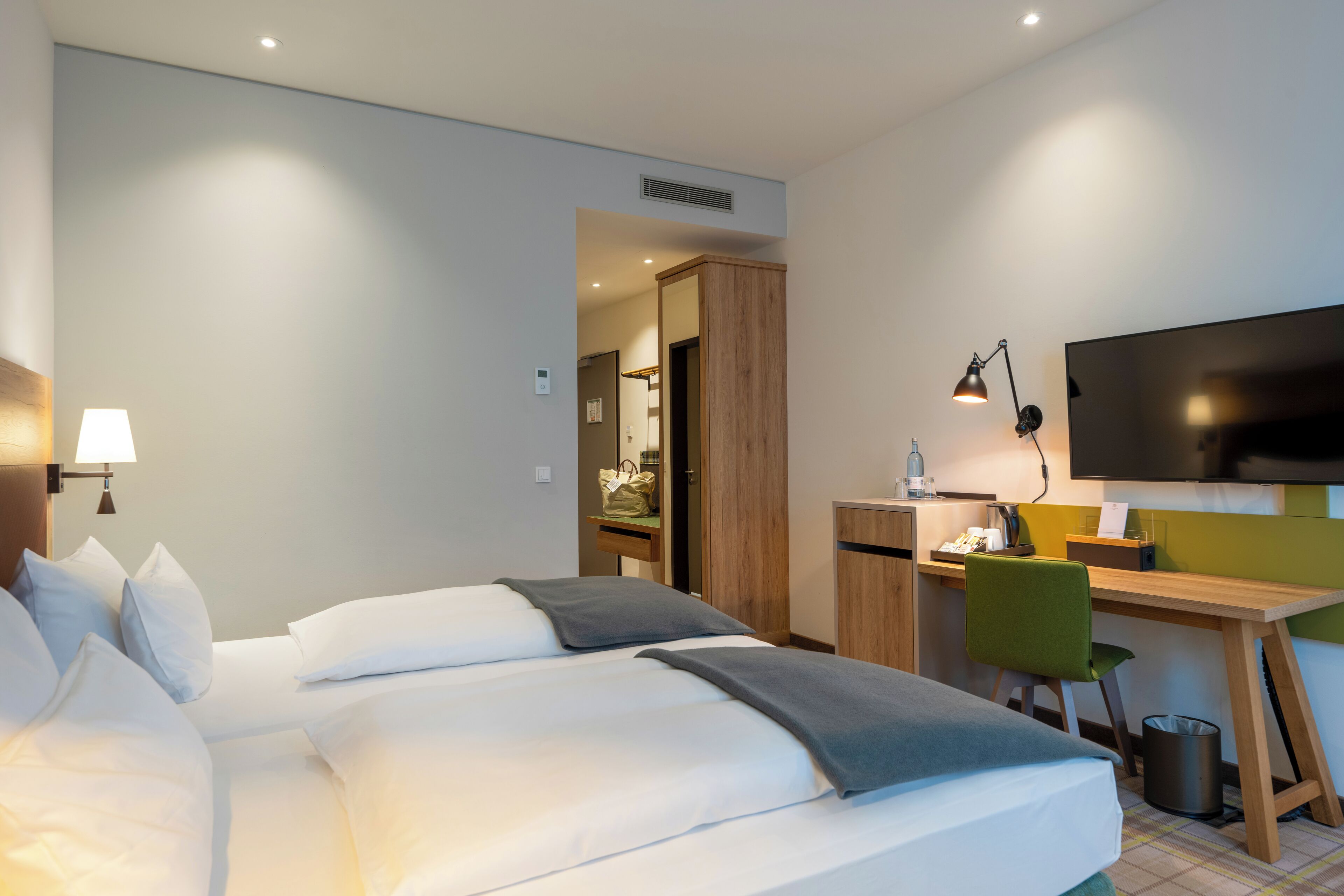 A hotel room with a bed, desk, chair, TV, lamp, and a trash can.