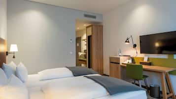 A hotel room with a bed, desk, chair, TV, lamp, and a trash can.