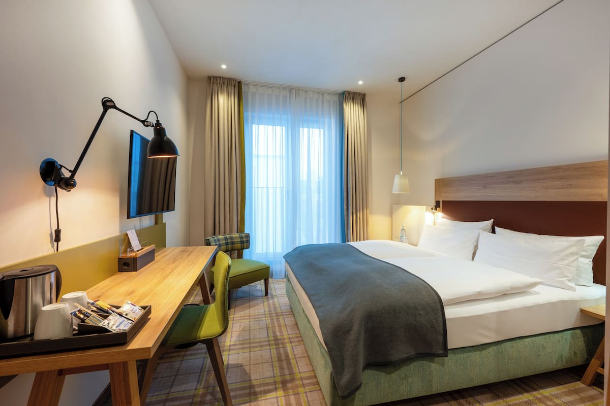 Una habitación de hotel con una cama, un escritorio con silla, una cafetera y un televisor.