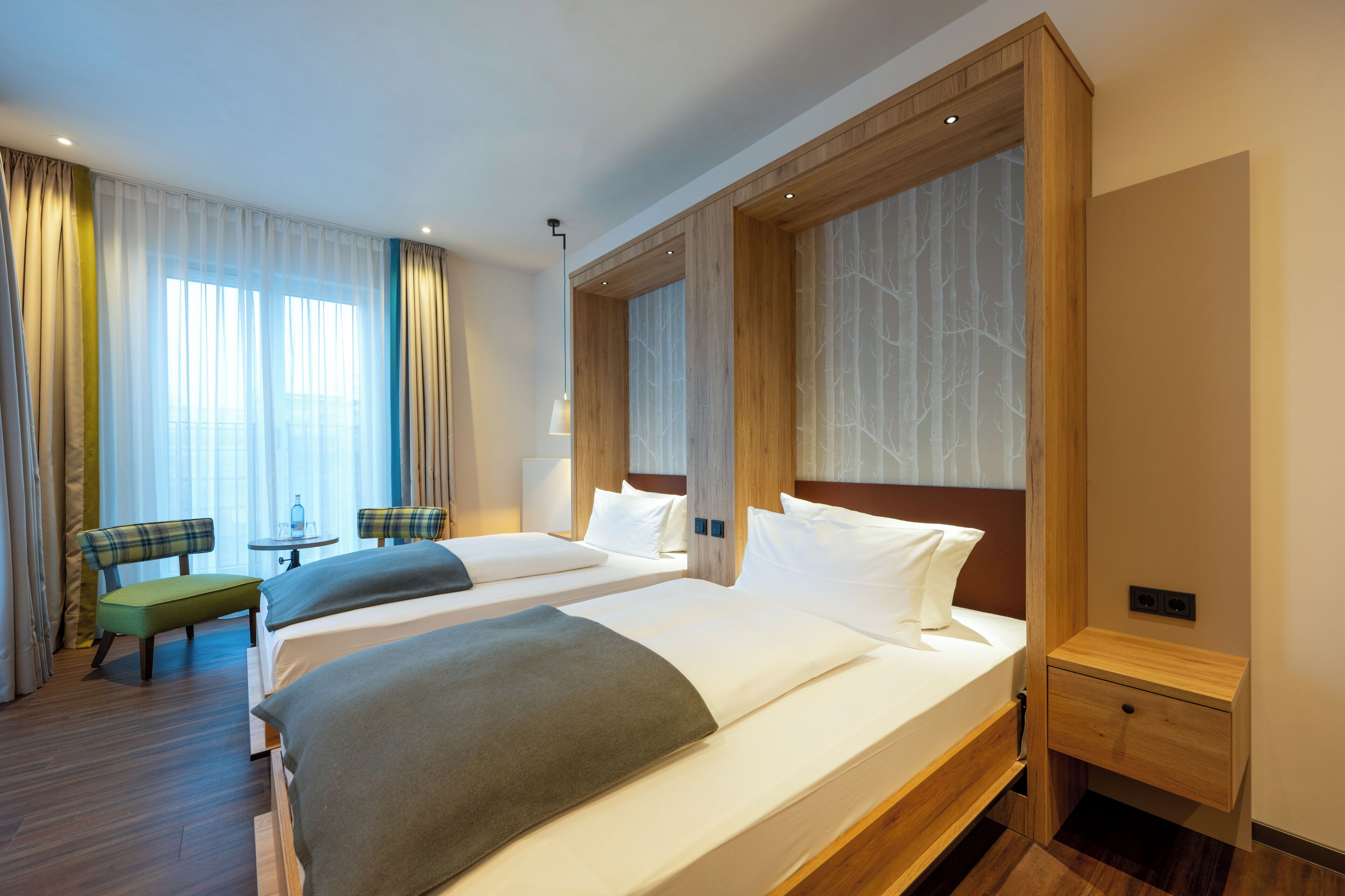 Camera d'albergo con due letti, un tavolino, una sedia e un comodino.